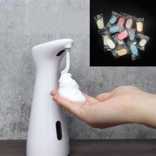 Hands holding a white automatic soap dispenser with colorful hand soap tablets visible in the background on a dark surface.