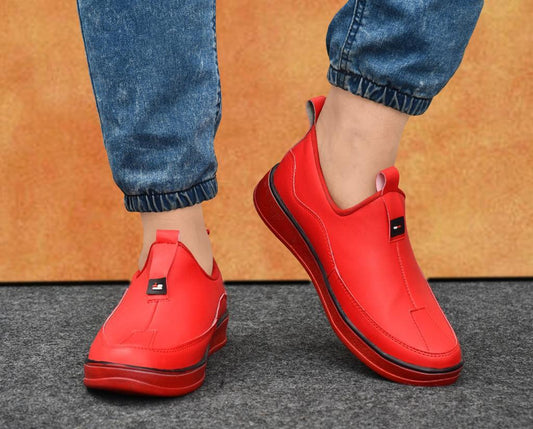 Stylish red casual shoes by Eliteshoppings on model's feet against orange background
