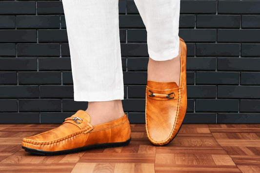 Stylish casual slip-on loafer shoes in warm orange hue on a wooden floor with a dark brick backdrop